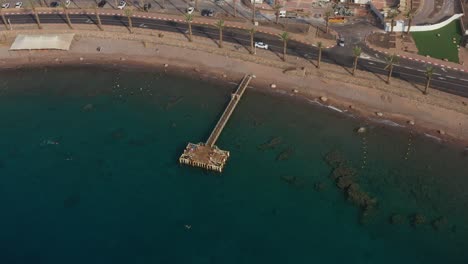 Panorámica-De-La-Vista-De-Drones-Moviéndose-A-Través-De-Un-Parque-Marino-Protegido-De-Arrecifes-De-Coral-Y-Aguas-Cristalinas-Famosas-Bajo-Un-Largo-Muelle-Para-El-Turismo,-El-Buceo-Y-La-Observación-De-La-Vida-Marina-En-El-Mar-Rojo-Eilat-Israel