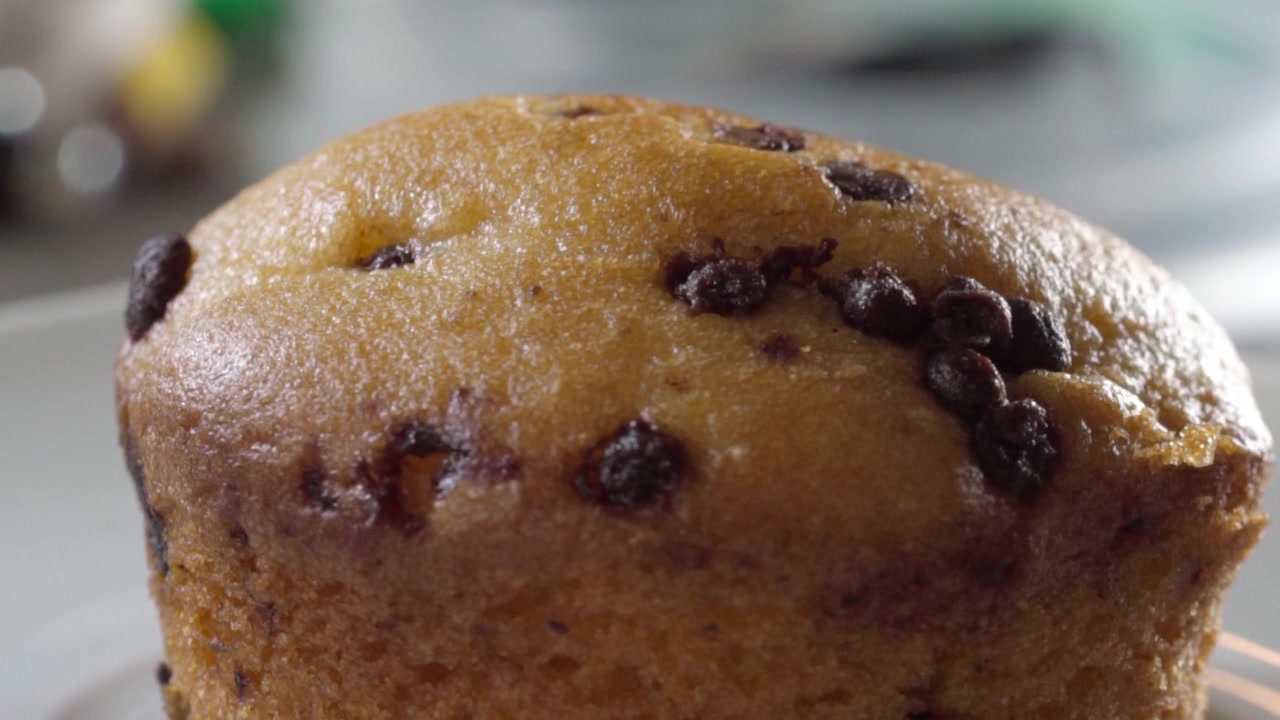Ripresa orbitale di un muffin ai pezzi di cioccolato appena sfornato, che evidenzia la sua consistenza morbida, la crosta dorata e le ricche gocce di cioccolato in una presentazione alimentare in primissimo piano.