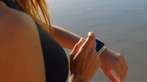 mujer en forma usando reloj inteligente en la playa 4k