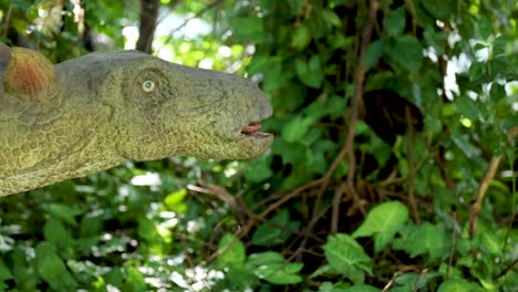 A dinosaur model appears in dense foliage, creating a lifelike prehistoric scene with natural lighting and static camera