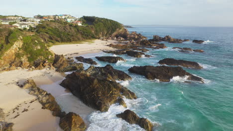 Waves-retracing-from-rocky-Australian-coastal-beach,-backwards-aerial-view