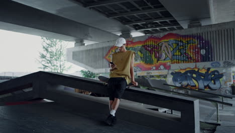 stylish skater browsing internet online on mobile phone at skatepark graffiti.