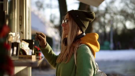 Woman-choosing-goods-in-street-kiosk-on-winter-walk,-waiting-for-order