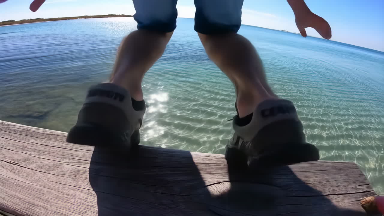 Man jumps into clear ocean water from a pier