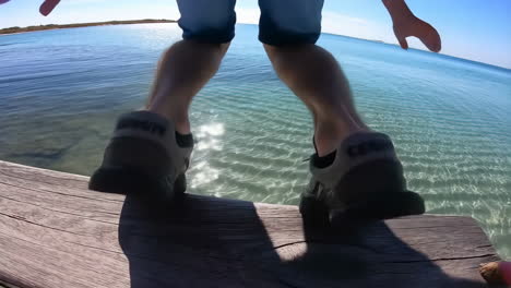 man jumps into clear ocean water from a pier