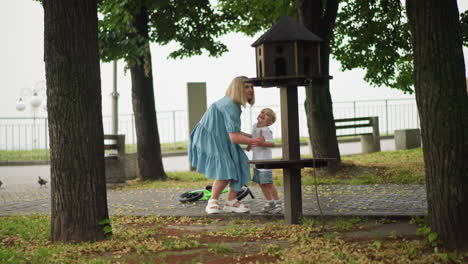 a mother lovingly holds her young son s hand, pointing to a birdhouse while they stand in a park, the boy s bicycle rests on the ground nearby