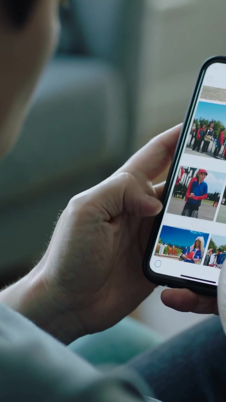 Vertical video: Browsing man in light top tapping phone and scrolling thumbnail grid on couch