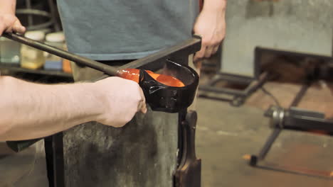 two glass artists form red hot molten glass by rotating inside a mold