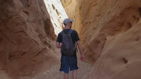 following a young man wearing a hat, backpack, t-shirt, and shorts through a slot canyon in southern utah