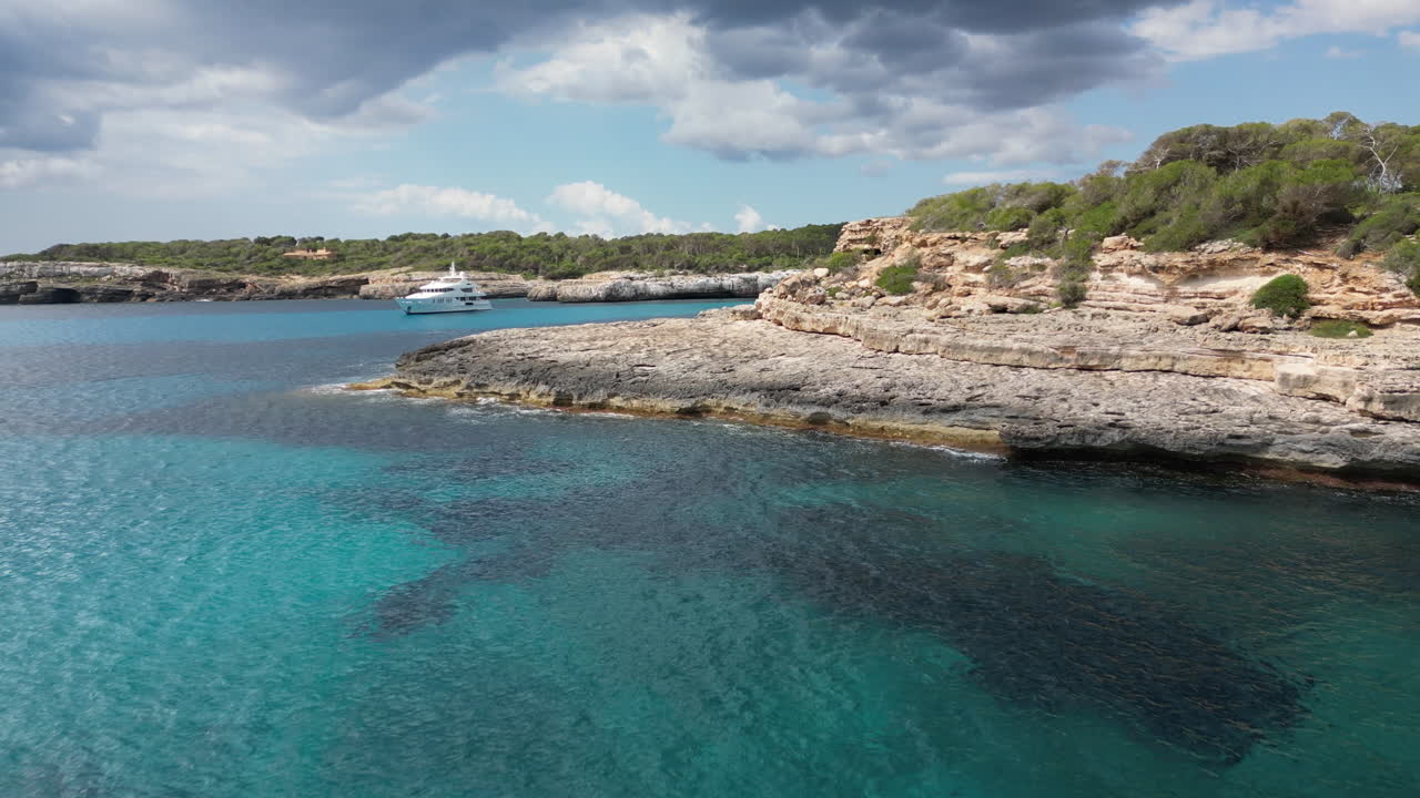 Spectacular 4K drone footage of Mallorca’s wild coastline, showcasing clear turquoise sea, steep cliffs, and golden sunlight dancing on the waves as they break along the rugged shore