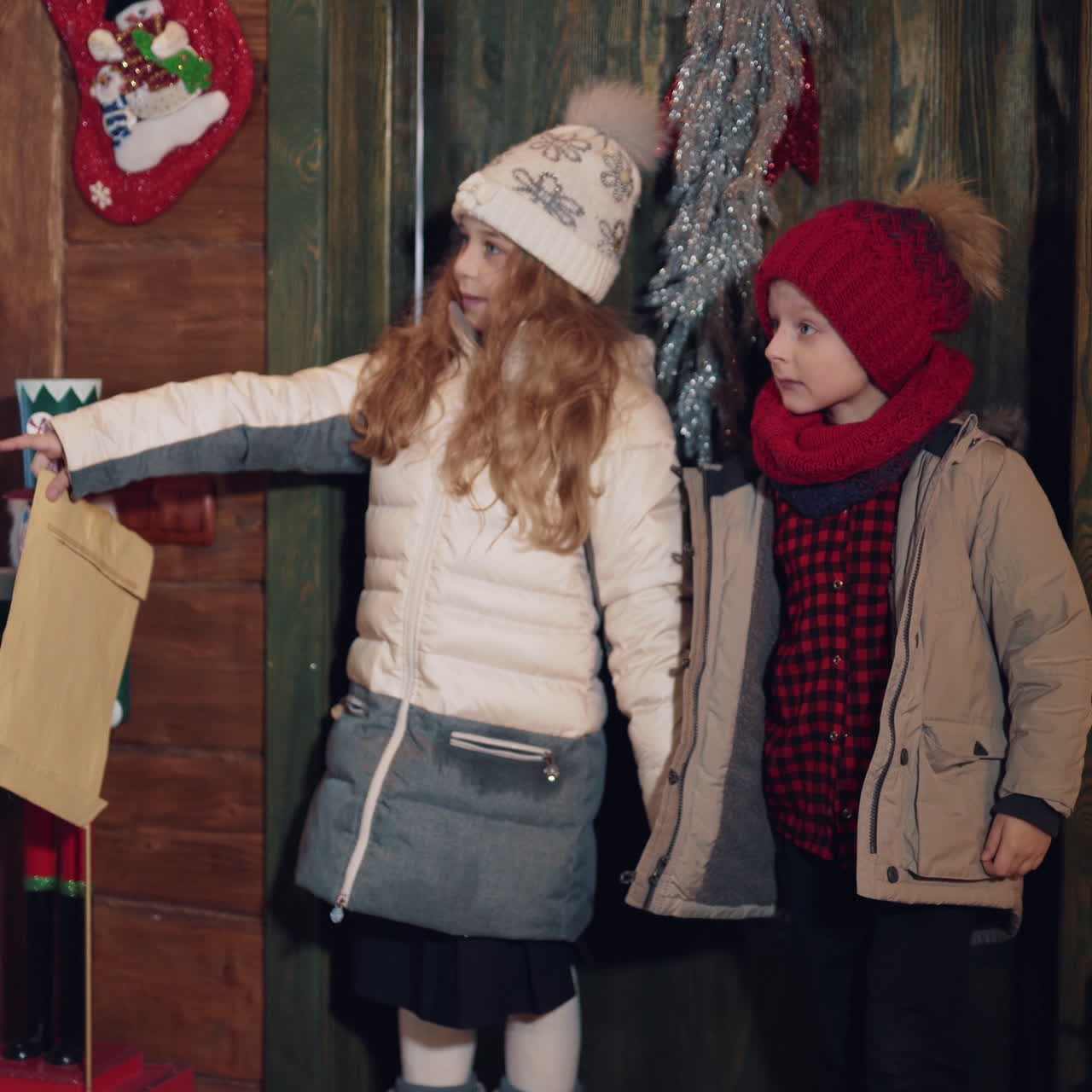 Little boy and girl with envelope coming into Santas residence. Children looking wonderingly inside the decorated house at Christmas.