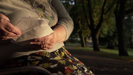 Mature-woman-reading-letter-in-the-park-zoom-out-shot