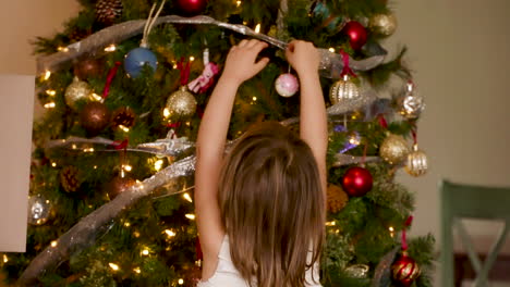 little girl hanging ornaments on a christmas tree