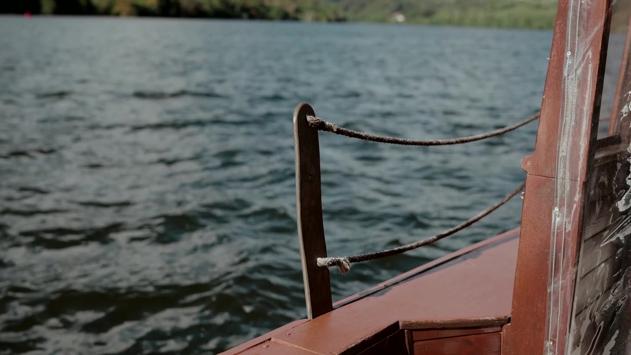 Hölzernes Bootsdeck mit an dunklem Pfosten befestigtem Seil und unruhigem blauem Flusswasser im Hintergrund an Bord