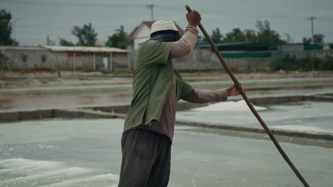 A Salt Farmer Working in Traditional Salt Fields Under an Overcast Sky