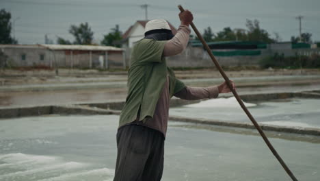 a salt farmer working in traditional salt fields under an overcast sky