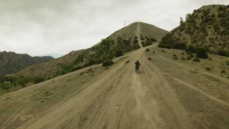 motorcyclist walkthroughs difficult track in hilly valley fpv. sportsman rides motorbike along dusty trail at highland site. extreme sport competition