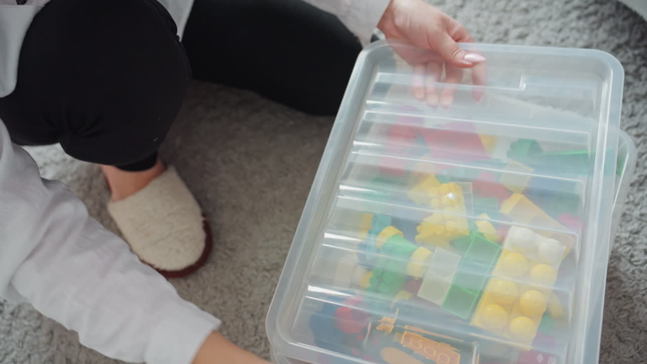 Forælder organiserer legetøj. Mor arrangerer omhyggeligt legetøj. Kvinde sorterer systematisk farverige legetøjsdele. Forælder og omsorgsperson organiserer og opbevarer metodisk farverigt legetøj efter legetid.
