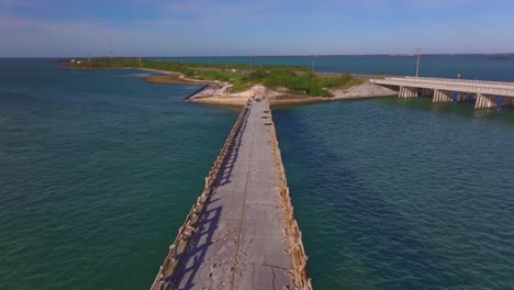 Progression of an old, deteriorating bridge over clear blue water with a modern highway bridge in the background
