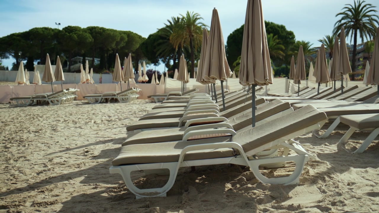 Deserted sandy beach with rows of sun loungers and folded parasols, evoking peace and solitude during off-season travel