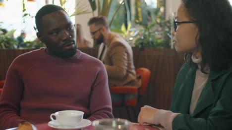 african american man speaking with asian female colleague in cafe