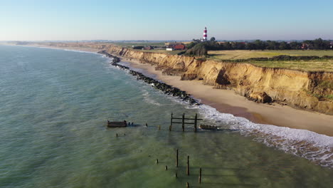 Stetige-Aufnahmen-Von-Drohnen-Der-Küstenverteidigung-In-Happiburgh,-Norfolk,-Großbritannien,-Mit-Dem-Leuchtturm-Im-Hintergrund