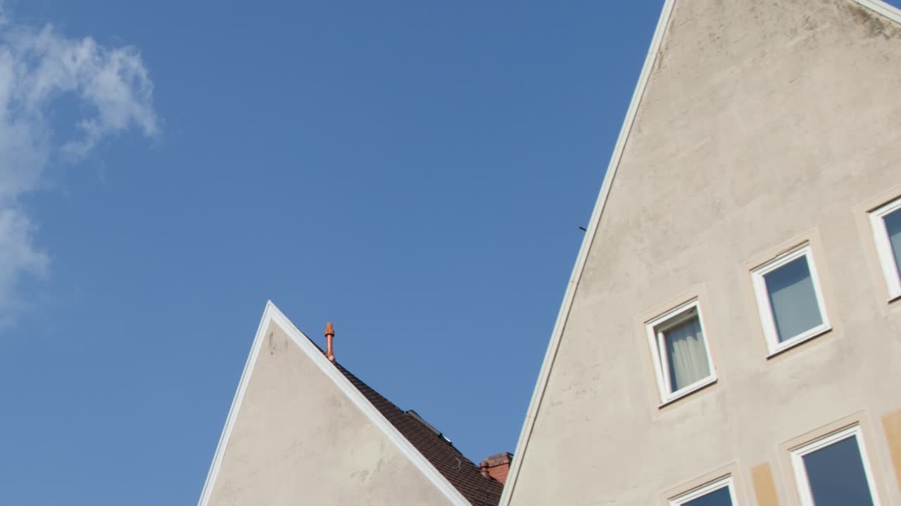 Camera tilts upward revealing modern gabled building facade in bright daylight, clear sky background