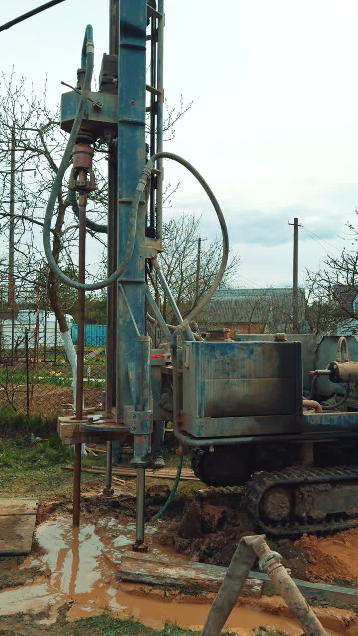 Boring a water well in the countryside household. Drilling equipment rotates the nozzle in the muddy puddle. Vertical video.