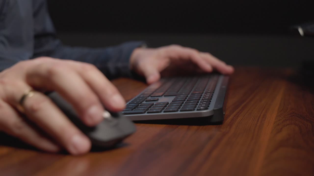 Person&rsquo;s hands using a computer mouse and keyboard on a wooden desk