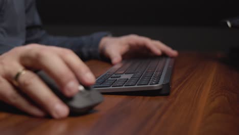 person’s hands using a computer mouse and keyboard on a wooden desk