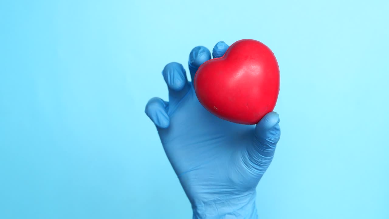 mano con guante azul sosteniendo un corazón rojo