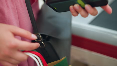 vista a mano de la dama buscando en su bolso para recuperar su teléfono, seguida de sacar una tarjeta de color limón, con una vista parcial de su bolsa de compras en su mano con un entorno borroso