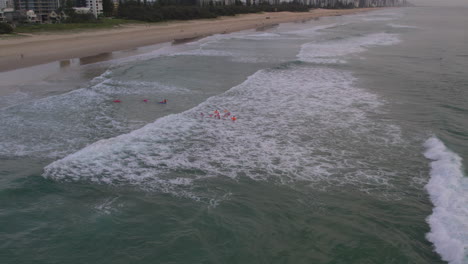 Vista-Aérea-De-Un-Grupo-De-Pinzas-Corriendo-Hacia-El-Agua-Durante-Una-Sesión-De-Entrenamiento-Matutina-Con-Vigilancia-De-Seguridad-En-El-Agua-En-Mermaid-Beach-Gold-Coast-Queensland-Australia