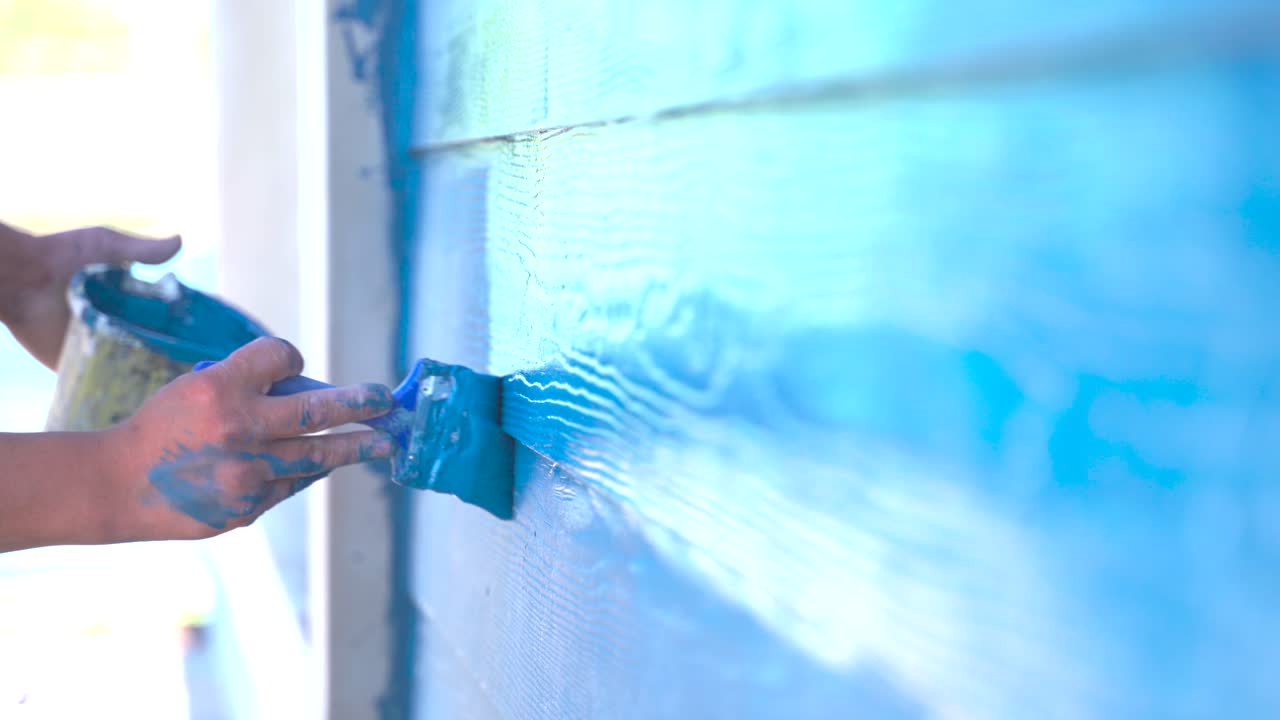 un primer plano de un hombre pintando a mano las paredes de madera con azul