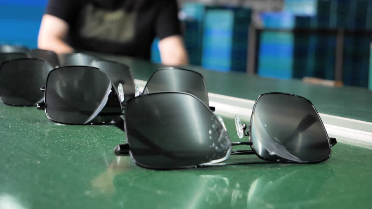 A person placing sunglasses onto a conveyor belt in a sunglasses factory in Danyang, Jiangsu Province, China. The slow-motion footage emphasizes the precision of the process.