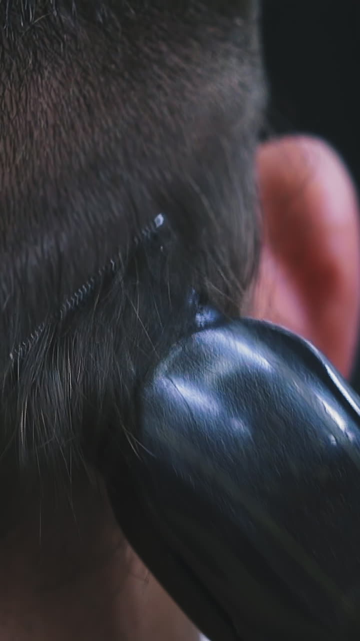 CU, slow motion: skilled barber does haircut to male client shaving black hair on head back with clipper machine in barbershop backside close view