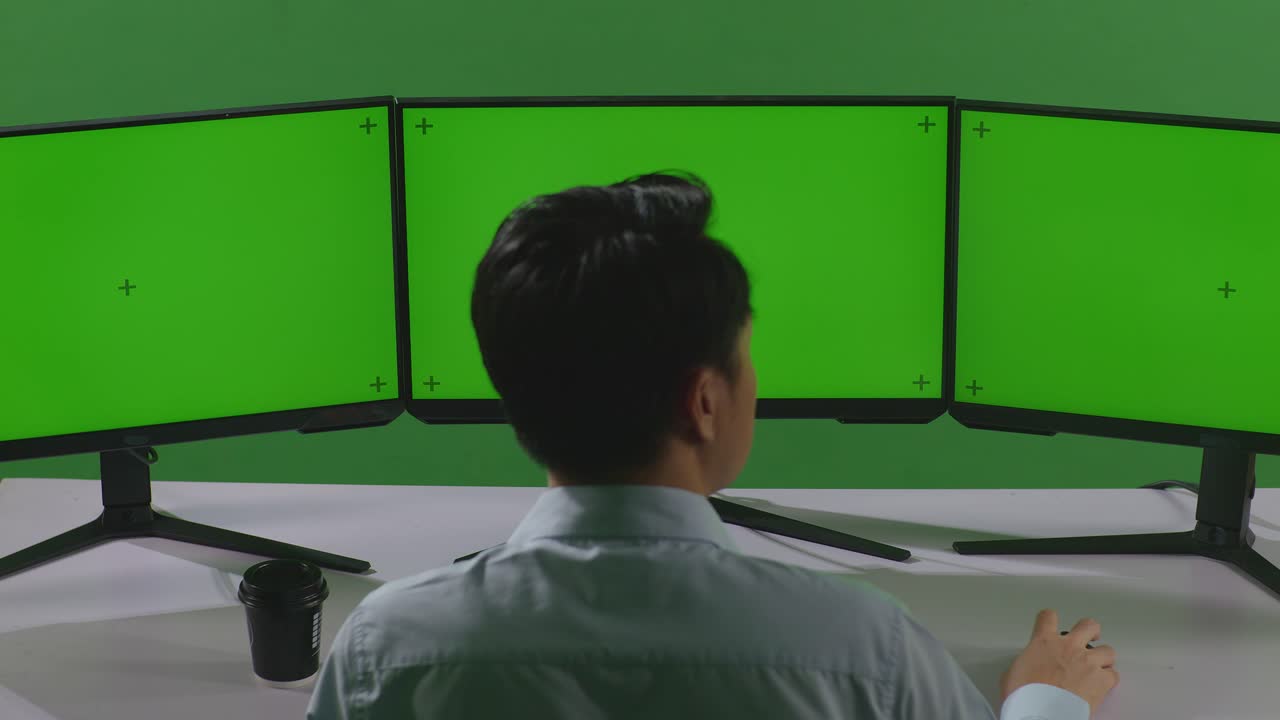 녹색 스크린 스튜디오에서 모의 다중 컴퓨터 모니터로 작업하는 동안 허리 통증이 있는 아시아 남자의 뒷면