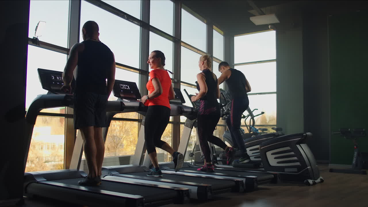 Young athletic men and women exercising and running on treadmill in sport gym.