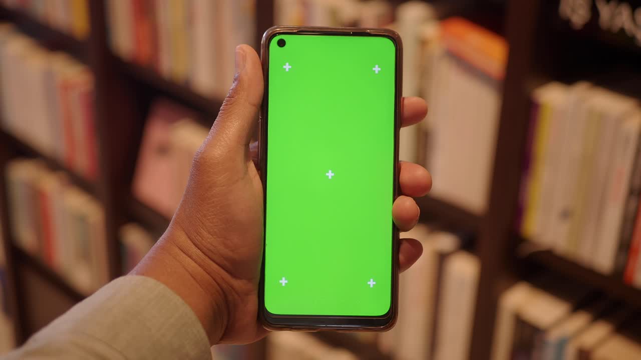 Mano che tiene un telefono con schermo verde davanti a una libreria