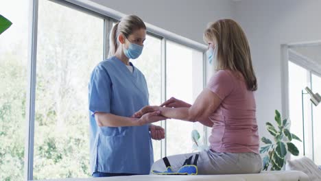 Female-health-worker-stretching-wrist-of-senior-woman-at-home