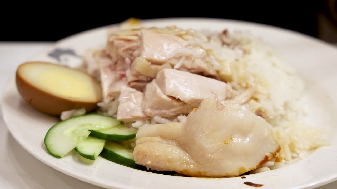 A close-up sequence of hands using a spoon and fork to pick up Hainanese chicken rice, sliced cucumber, and egg under bright indoor lighting