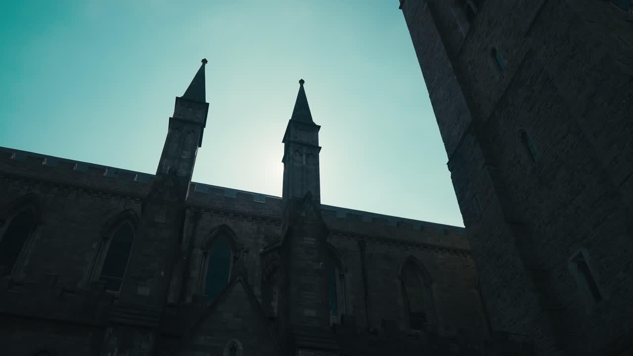 Silhouette of church steeples in front of sun flare and dramatic blue sky.