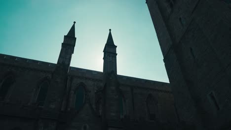 silhouette of church steeples in front of sun flare and dramatic blue sky.