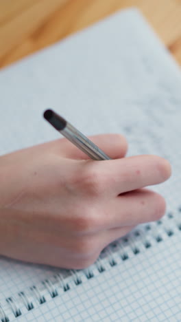 primer plano de un joven estudiante escribiendo a mano con una pluma en el cuaderno, vista parcial de una taza de café en la mesa, demostrando un momento de estudio enfocado con un fondo suave