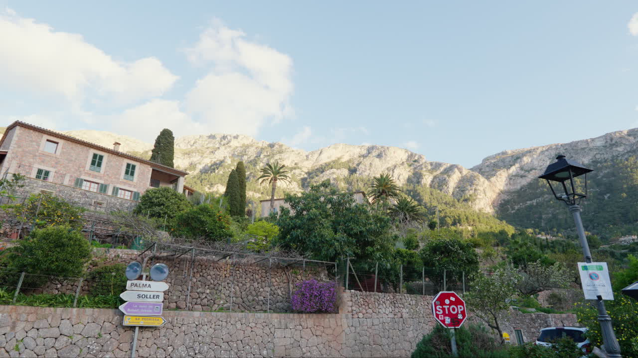 A street in De&iacute;a, Mallorca, Spain, framed by houses, plants, and mountains under a clear blue sky, creating a picturesque scene