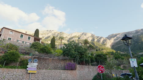 A-street-in-Deía,-Mallorca,-Spain,-framed-by-houses,-plants,-and-mountains-under-a-clear-blue-sky,-creating-a-picturesque-scene