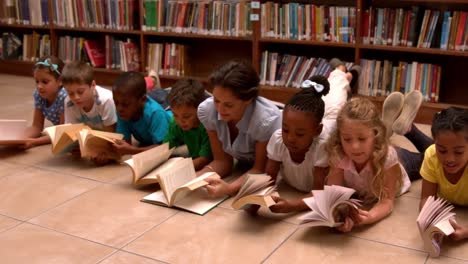 maestro y alumnos leyendo libros en el piso de la biblioteca