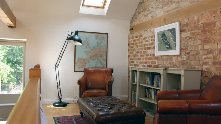 Mezzanino interno di una casa di lusso con mobili in pelle e libri in una biblioteca, con una parete in mattoni a vista e ampie finestre.
