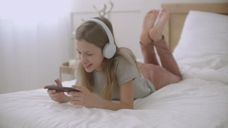 school girl is using app in smartphone lying in bedroom and talking leisure of children in weekend