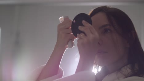 lady using a illuminated pocket mirror applies foundation makeup to her forehead